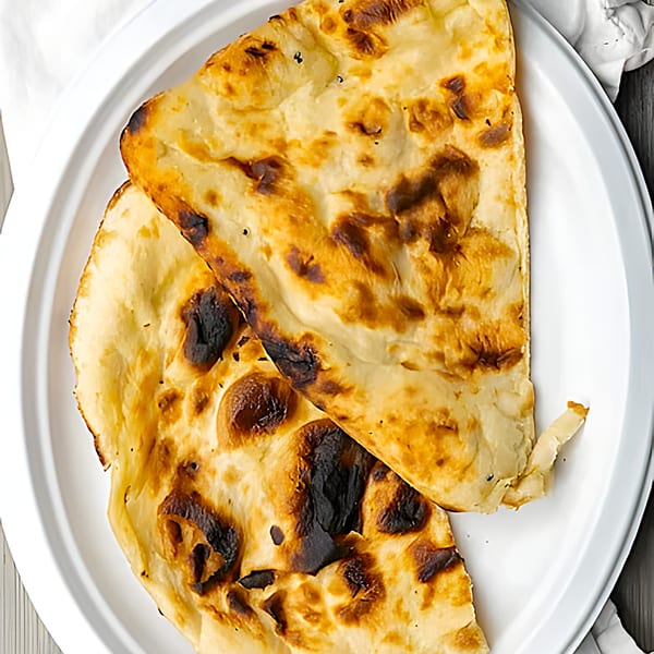 Two pieces of golden-brown naan bread with charred spots on a white plate.