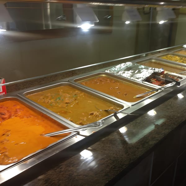 A buffet line at India Grill with several trays of Indian curries and other dishes.