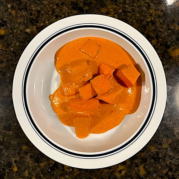 Overhead view of India Grill's paneer butter masala, featuring paneer cubes in a rich orange sauce.