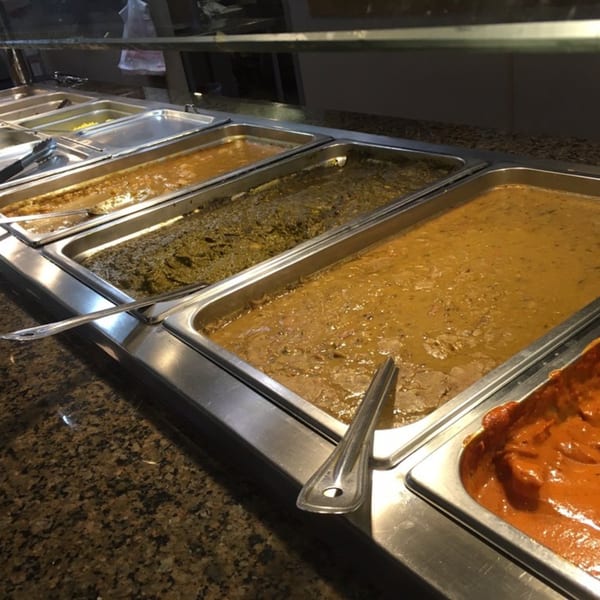 A buffet line at India Grill with various Indian dishes in metal serving trays.