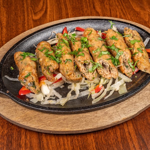 Six Indian seekh kebabs, garnished with fresh cilantro, served on a sizzling platter with onions and peppers.