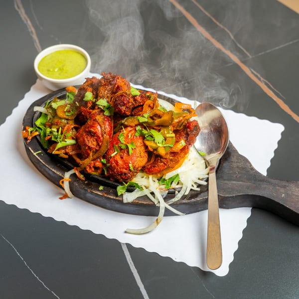 Steaming hot Indian Grill chicken tikka sizzler with onions, peppers, and cilantro, served with green chutney.