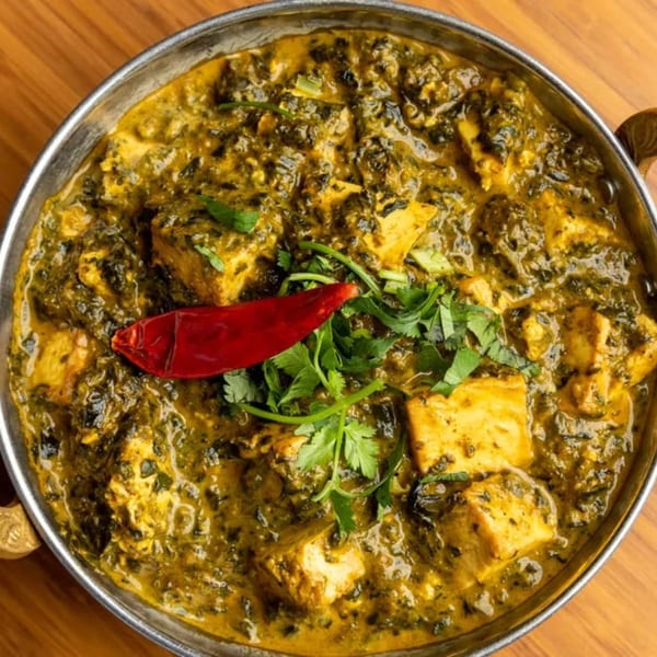 Close-up of India Grill's Palak Paneer, a vibrant green spinach and cheese curry, garnished with a red chili.