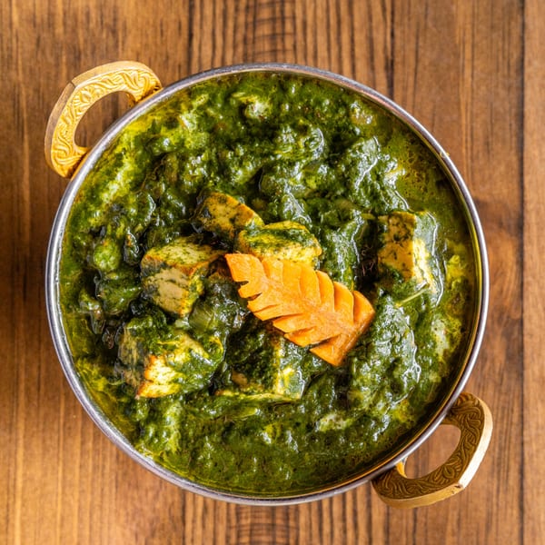 Palak Paneer, a vibrant green Indian dish with paneer cheese and a carrot garnish, in a metal bowl.